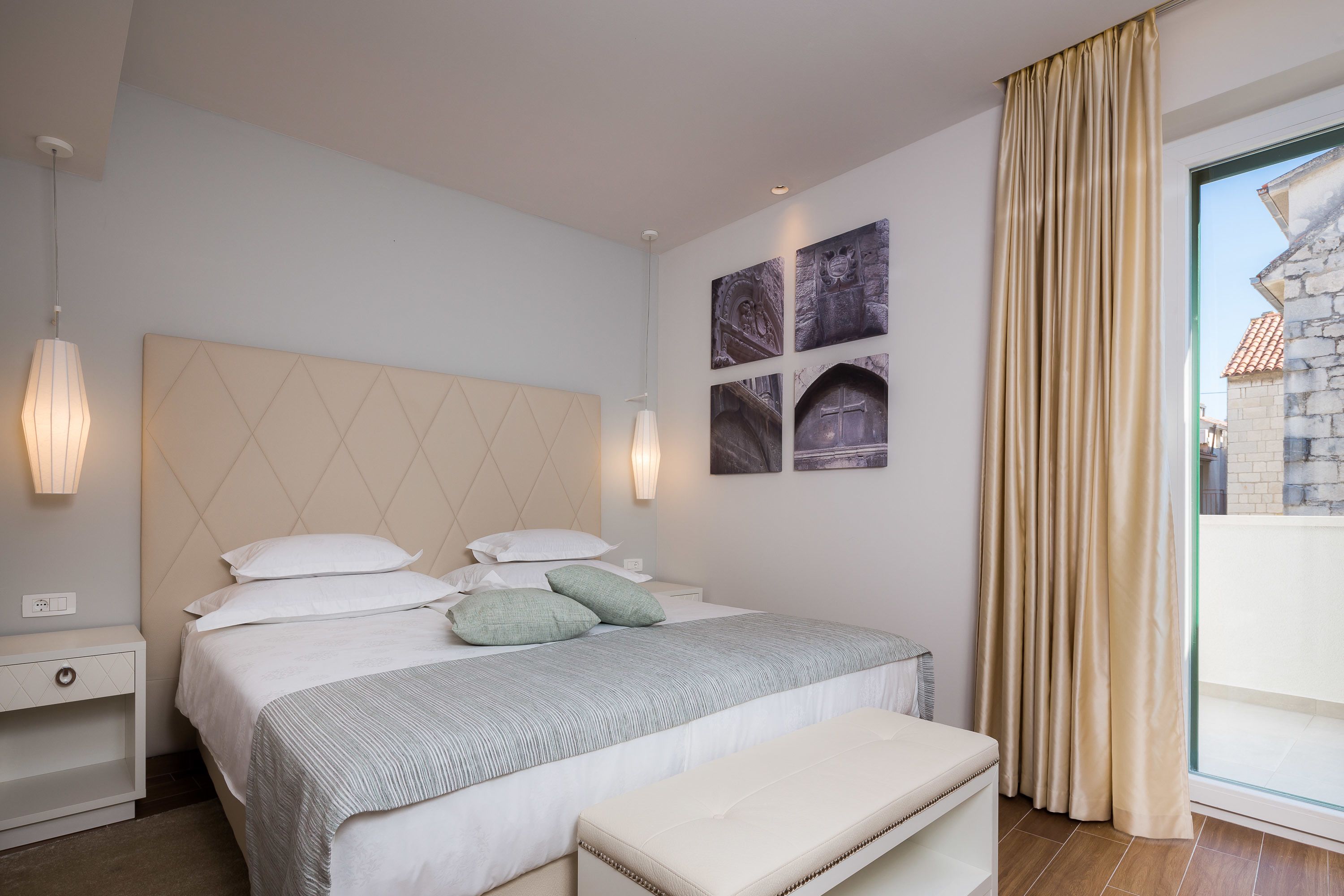 A modern bedroom with a large bed, bedside tables, a bench, and artwork on the wall.