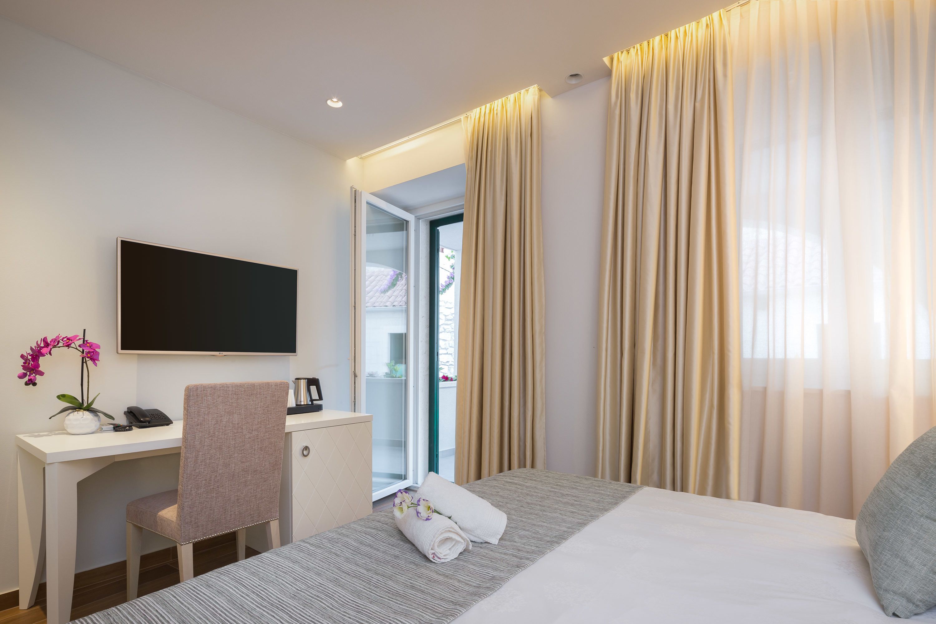 A hotel room with a bed, a desk, a chair, a TV, and a window with curtains.