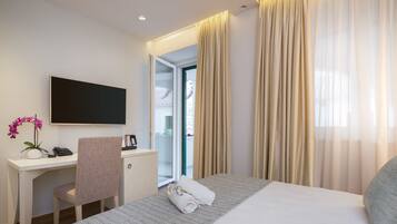 A hotel room with a bed, a desk, a chair, a TV, and a window with curtains.