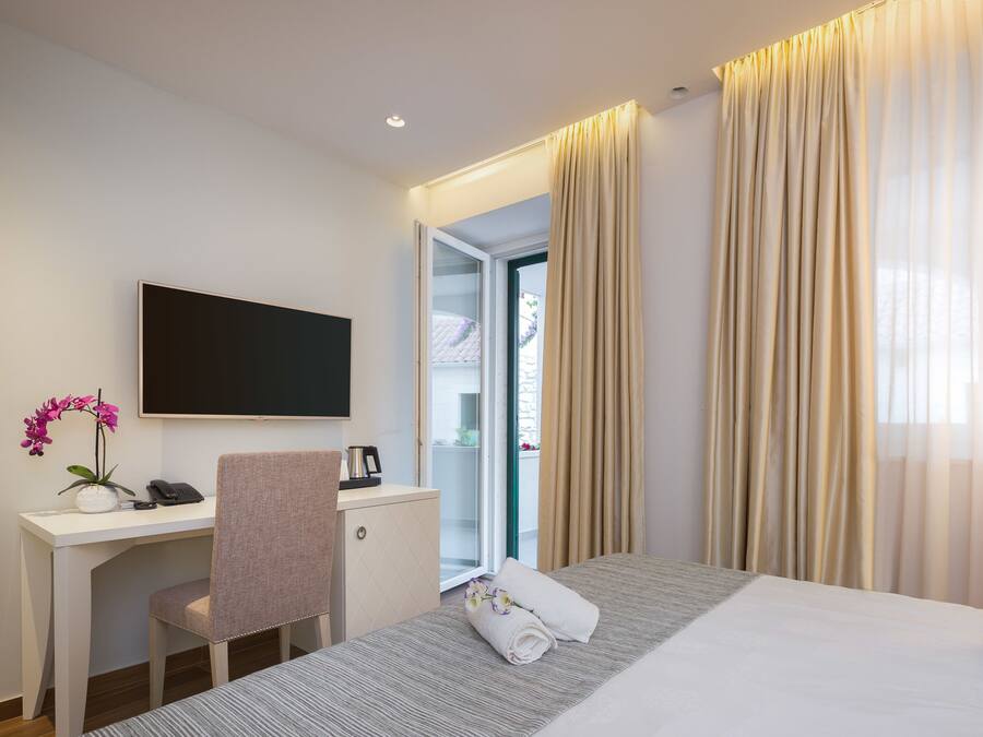 A hotel room with a bed, a desk, a chair, a TV, and a window with curtains.