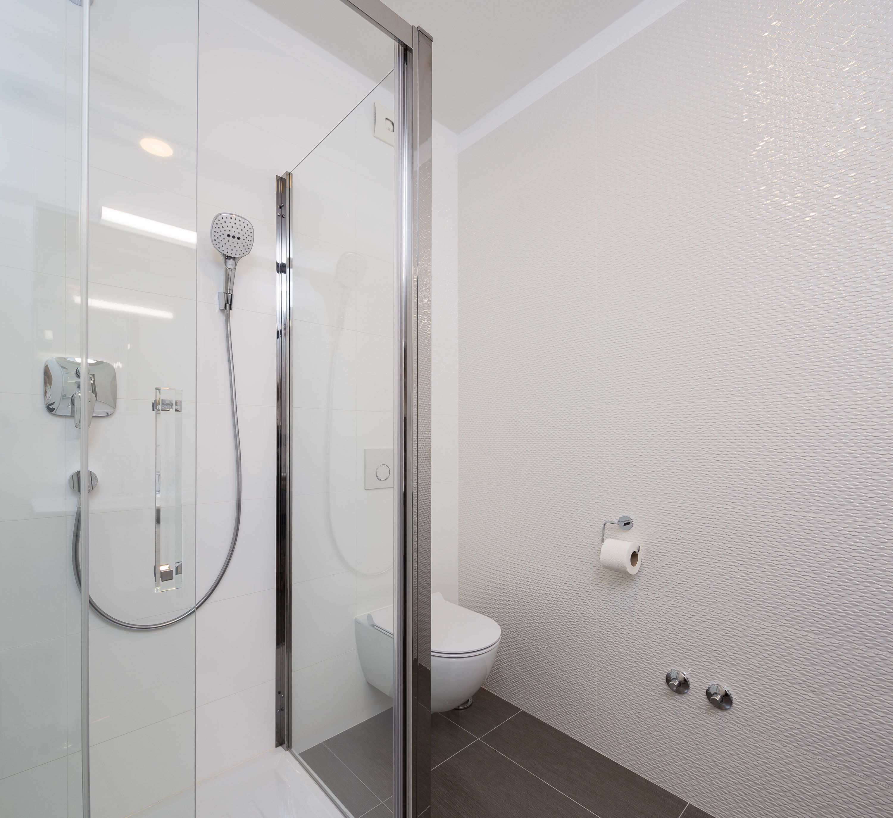 Une salle de bain moderne avec une douche à parois de verre, des toilettes et un mur à texture.
