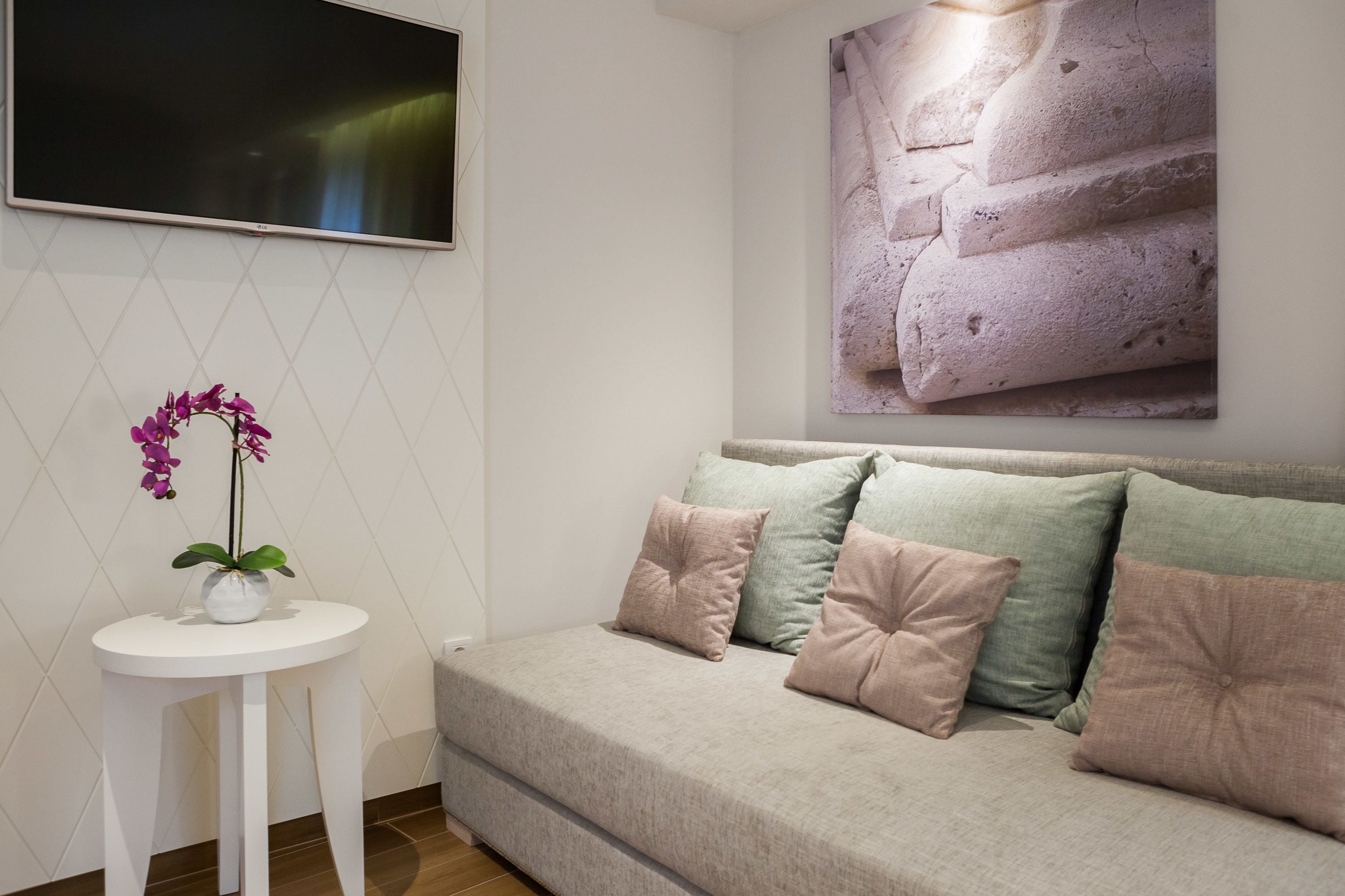 A modern living room with a beige sofa, a small white side table, and a purple orchid plant.