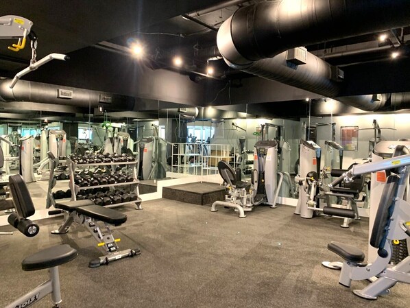 A gym with various exercise equipment, including dumbbells, benches, and weight machines. - Deluxe Beach Resort - HORA RENTALS (Miami Beach)