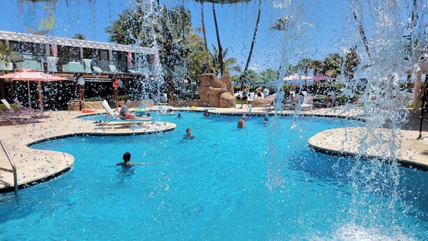 A swimming pool with multiple lanes, lounge chairs, and a lifeguard stand. - Deluxe Beach Resort - HORA RENTALS (Miami Beach)