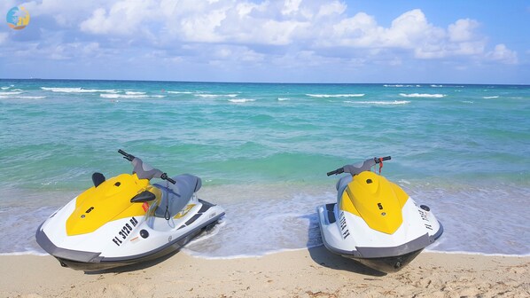 Two jet skis on a sandy beach with the ocean in the background. - Deluxe Beach Resort - HORA RENTALS (Miami Beach)