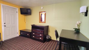 A room with a bed, a dresser, a desk, a chair, a television, and a window with curtains. - Desert Inn (Van Horn)