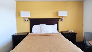 A hotel room with a large bed, two bedside tables, a nightstand, a lamp, and a chair. - Desert Inn (Van Horn)