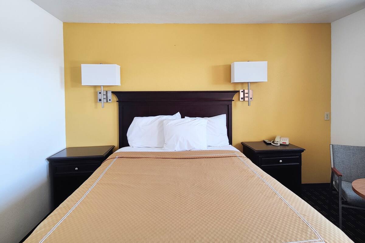 A hotel room with a large bed, two bedside tables, a nightstand, a lamp, and a chair.