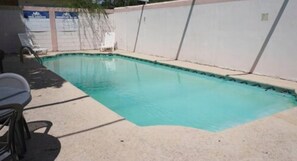 A swimming pool with a tiled deck, a lounge chair, and a white wall with a sign. - Hotel Maria Luisa Inn & Suites (Cadereyta Jimenez)