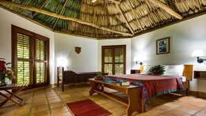 A room with a bed, a wooden table, a red rug, and a thatched roof ceiling. - Tanager Rainforest Lodge (Punta Gorda)