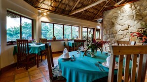 A dining area with tables set for four, large windows, and a stone wall. - Tanager Rainforest Lodge (Punta Gorda)