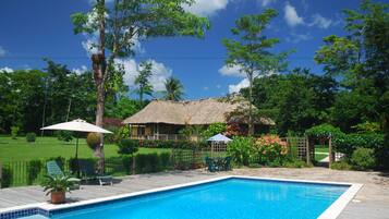 Relax by the pool surrounded by lush greenery and a thatched-roof structure.