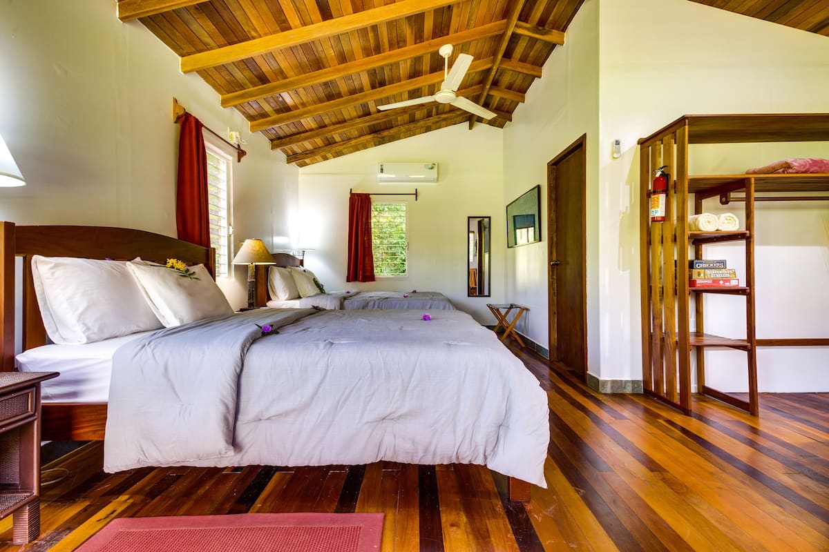 A bedroom with a wooden ceiling, a bed with white bedding, a bedside table, a lamp, and a wooden shelf with towels.