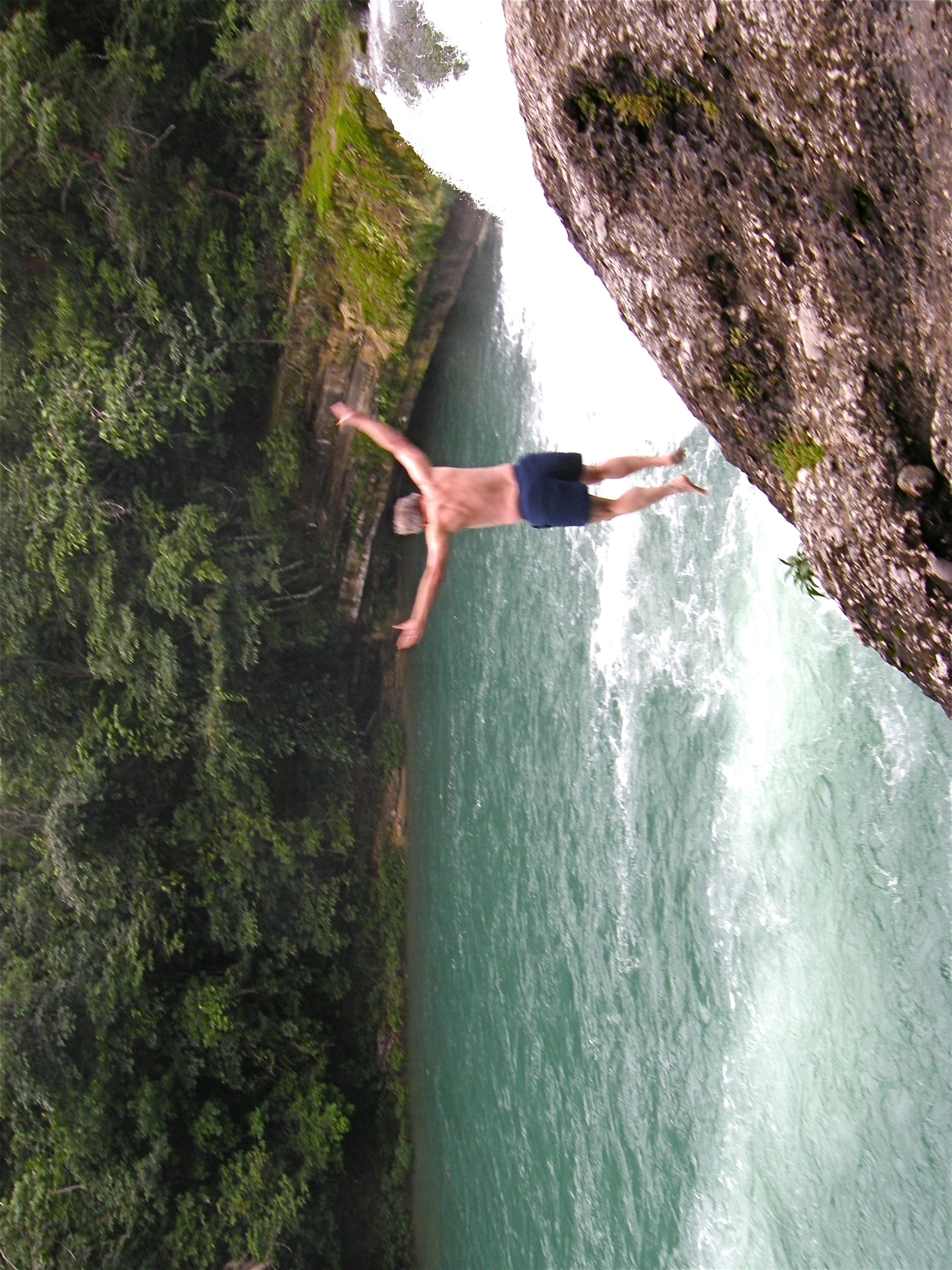 A person jumping off a cliff into a body of water surrounded by greenery.