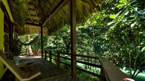 A wooden deck with a thatched roof, overlooking lush greenery. - Tanager Rainforest Lodge (Punta Gorda)