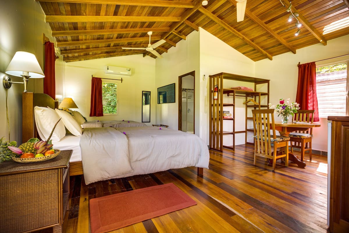 A bedroom with a wooden ceiling, a bed with white linens, a bedside table with a lamp, and a fruit basket.