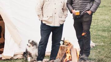 Deux personnes se tiennent près d’une tente, à côté d’un feu de camp.