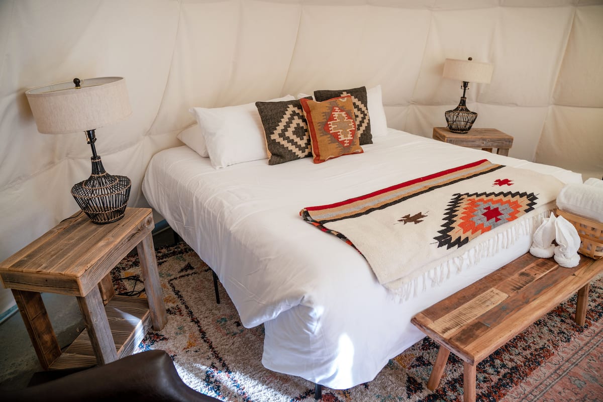 A neatly arranged bedroom with a large bed, two bedside tables, a bench, and a patterned rug.