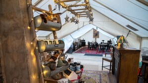 Una habitación con carpa decorada en estilo rústico, que incluye una estantería de madera con juguetes suaves, una alfombra estampada y una mesa con diversos objetos.