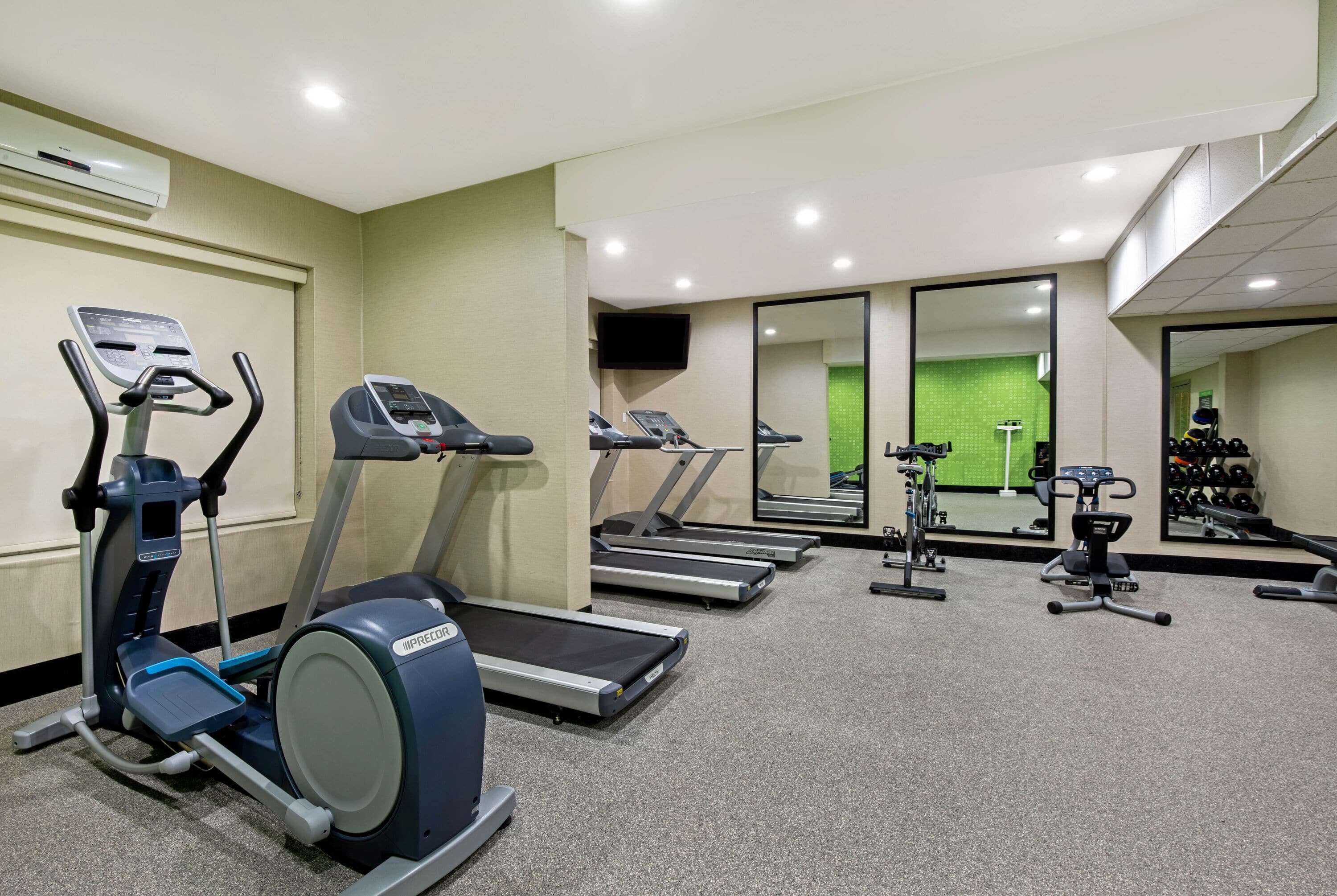 Une salle de sport équipée de tapis de course, d’un appareil elliptique et d’un banc de musculation.
