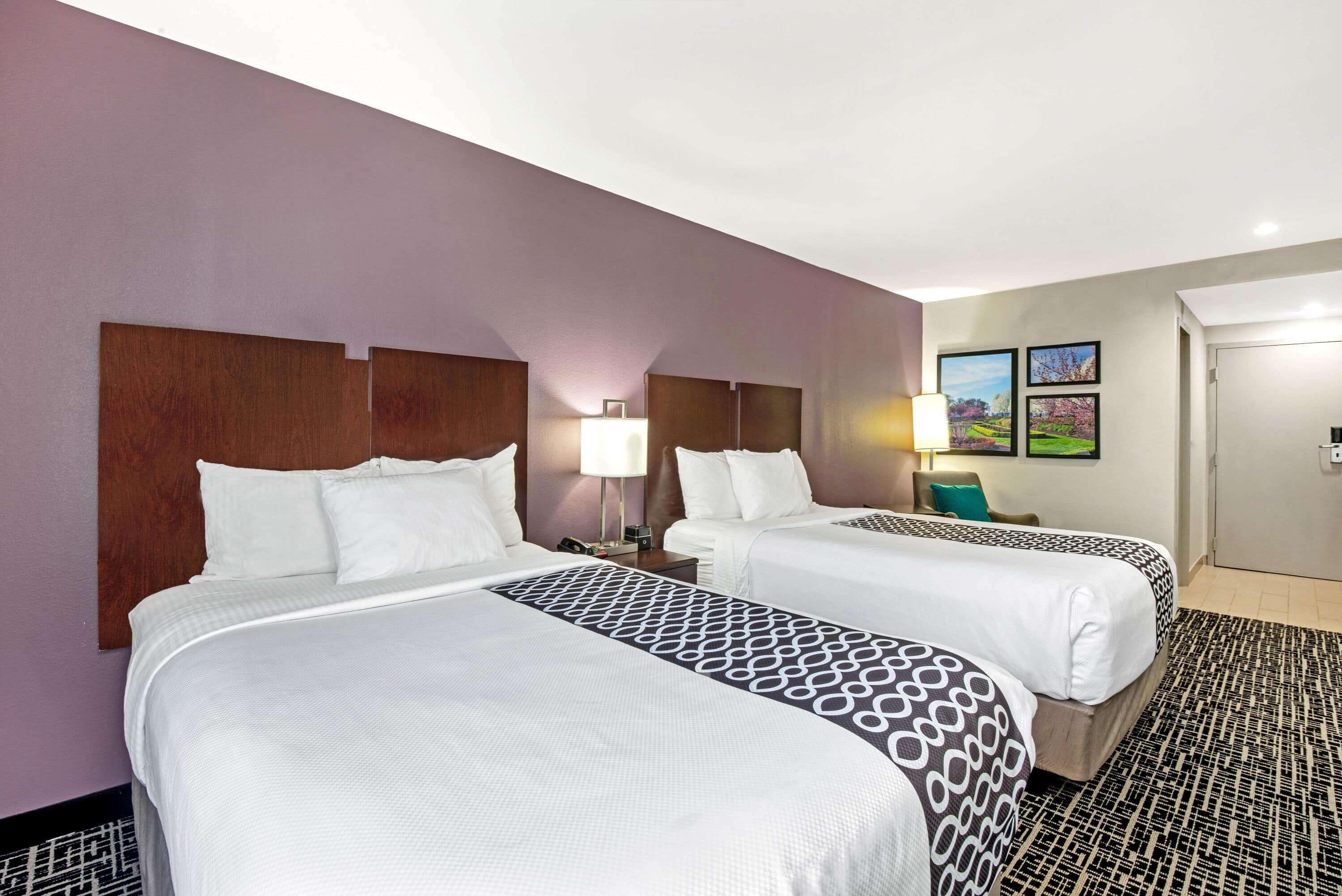 Een hotelkamer met twee bedden, een nachtkastje, een lamp en wanddecoraties in lijsten.