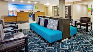 A hotel lobby with a reception desk, seating area, and a refrigerator stocked with beverages.