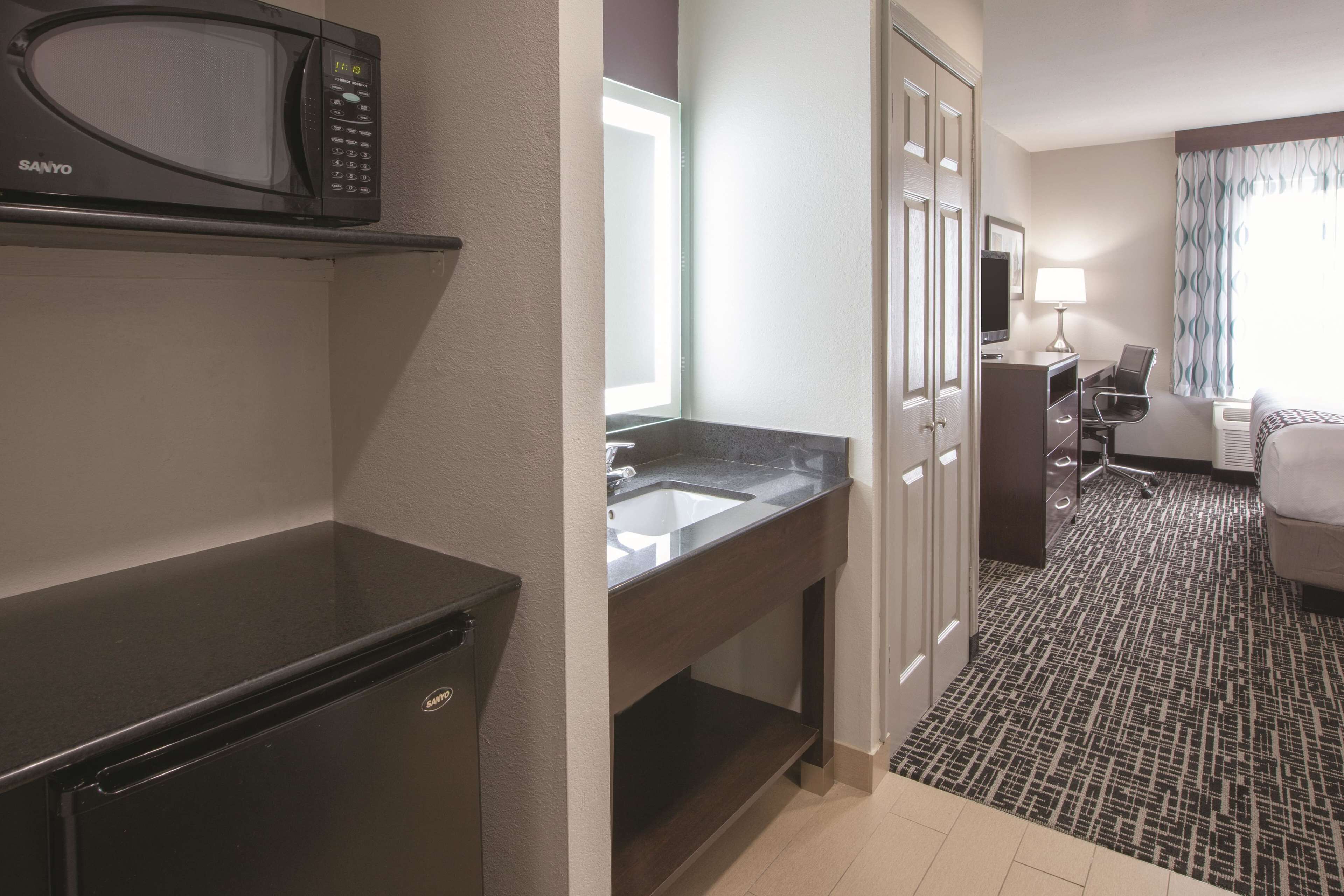 A hotel room with a kitchenette, including a microwave, refrigerator, and sink.