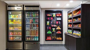 A vending area with two refrigerated display cases and shelves stocked with snacks and beverages.