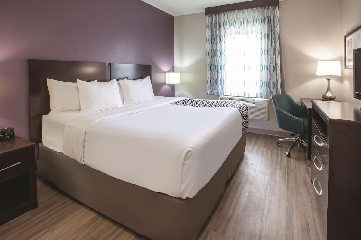 Une chambre d’hôtel avec un grand lit, un bureau avec une chaise, une lampe et une fenêtre avec des rideaux.