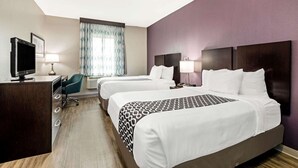 A hotel room with two beds, a desk with a computer, a TV, and a window with curtains.