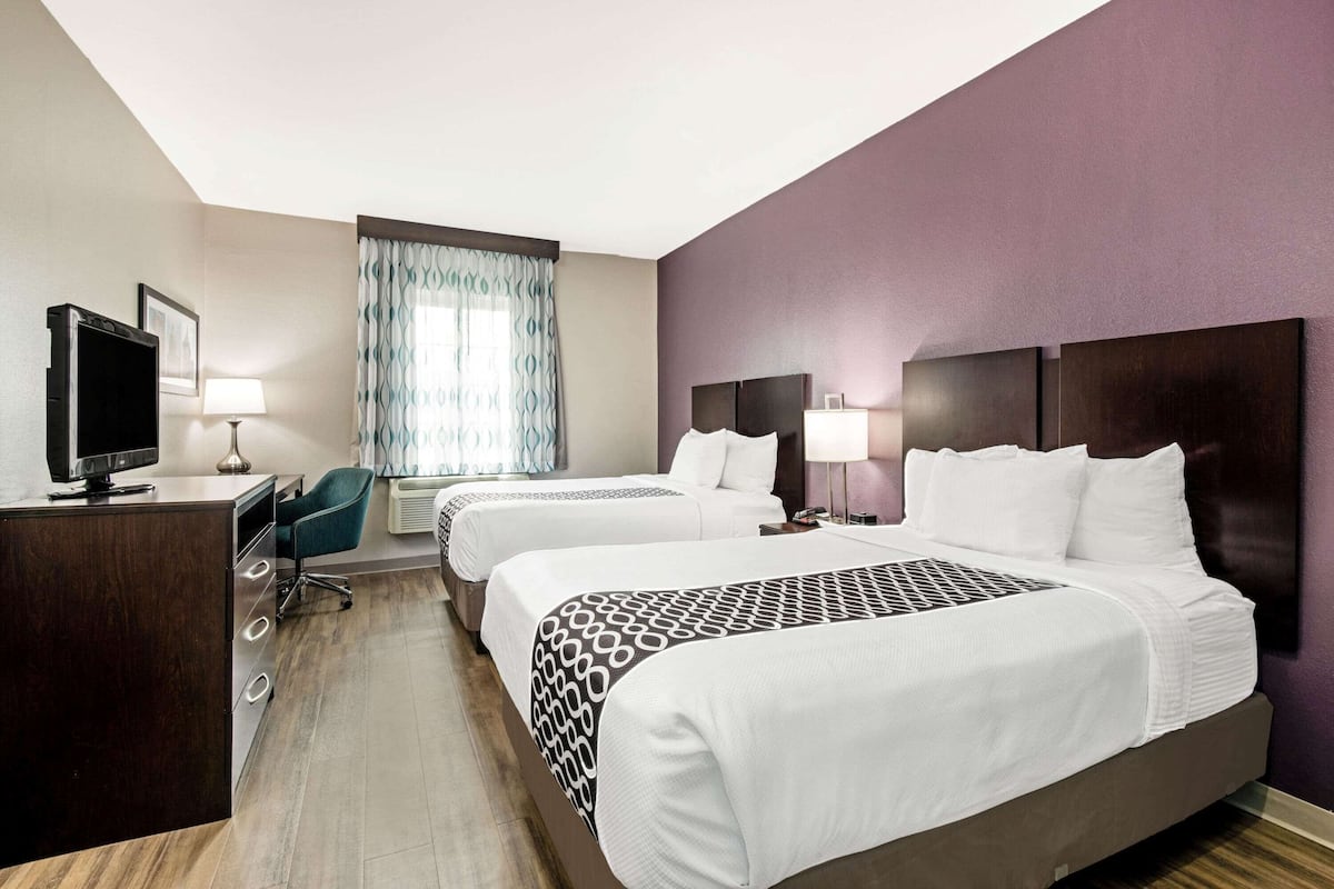Une chambre d’hôtel avec deux lits, un bureau avec un ordinateur, une télévision et une fenêtre avec des rideaux.