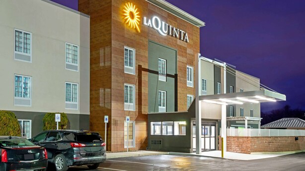 A La Quinta hotel with a modern design, featuring a prominent sun logo, multiple windows, and a covered parking area.