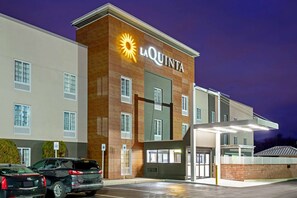 A La Quinta hotel with a modern design, featuring a prominent sun logo, multiple windows, and a covered parking area. - La Quinta Inn & Suites by Wyndham New Cumberland-Harrisburg (New Cumberland)