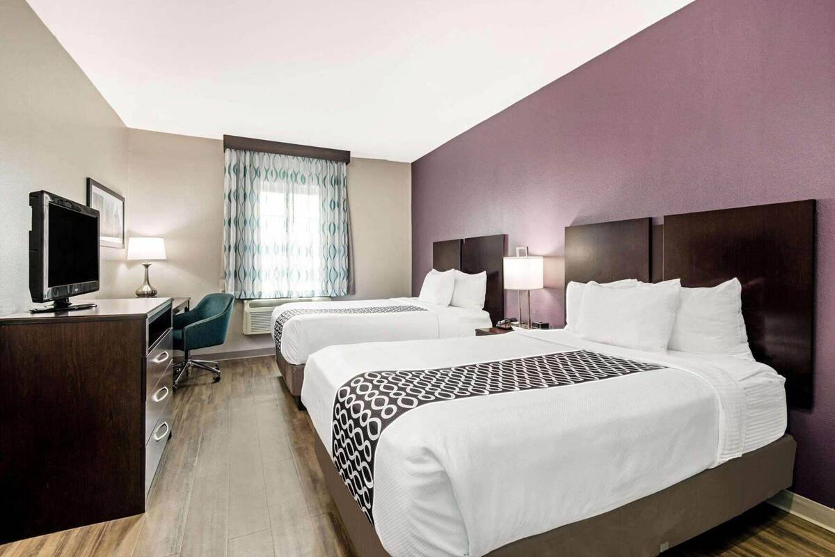 Une chambre d’hôtel avec deux lits, un bureau avec une télévision, une chaise et une fenêtre avec des rideaux.