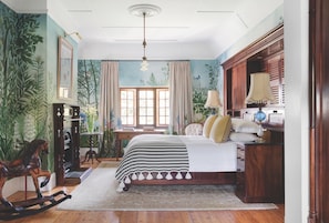 A bedroom with a bed, wooden rocking horse, and a desk with a lamp.