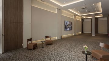 A spacious hotel lobby with a patterned carpet, seating areas, and a large screen displaying a video.
