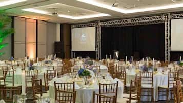 Uma sala de banquetes com mesas redondas preparadas para refeições, equipada com cadeiras e louças.