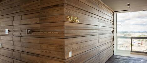 Parede de madeira com a placa "SAUNA", porta de vidro que dá para o exterior e vista da cidade.