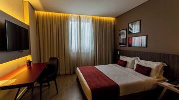 A hotel room with a bed, a desk, a chair, a TV, and curtains.