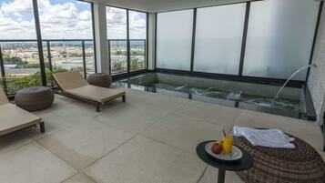 Relax on the spacious balcony with unobstructed city views, featuring comfortable seating and a luxurious hot tub.