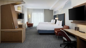 Ett hotellrum med en stor säng, ett skrivbord, en stol, en TV och en skrivbordslampa.