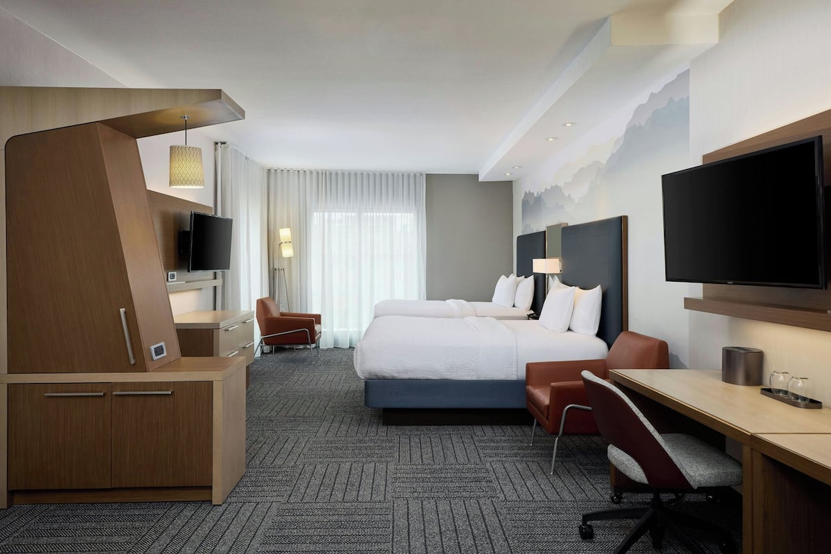A hotel room with a large bed, a desk, a chair, a TV, and a desk lamp.