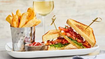 A plate with a grilled sandwich, a glass of white wine, and a small container of ketchup.