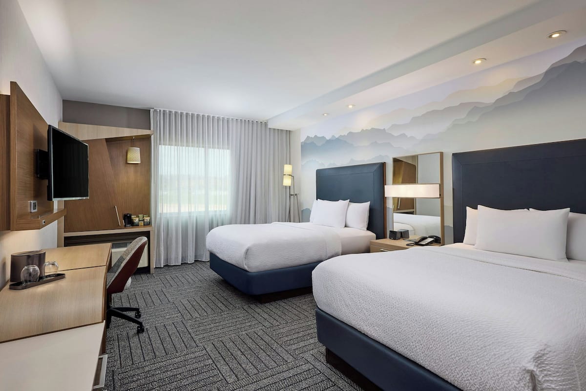 A hotel room with two beds, a desk, a TV, and a bathroom.
