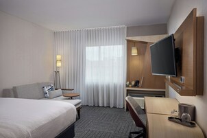 Une chambre d’hôtel avec un lit, un bureau, une télévision et une fenêtre avec des rideaux.