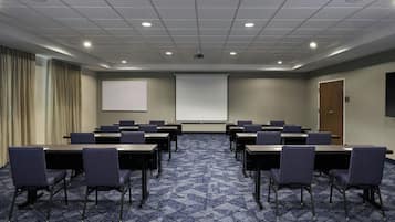 Ein Konferenzraum mit Projektionsleinwand, mehreren Tischen und Stühlen, bereit für Besprechungen.