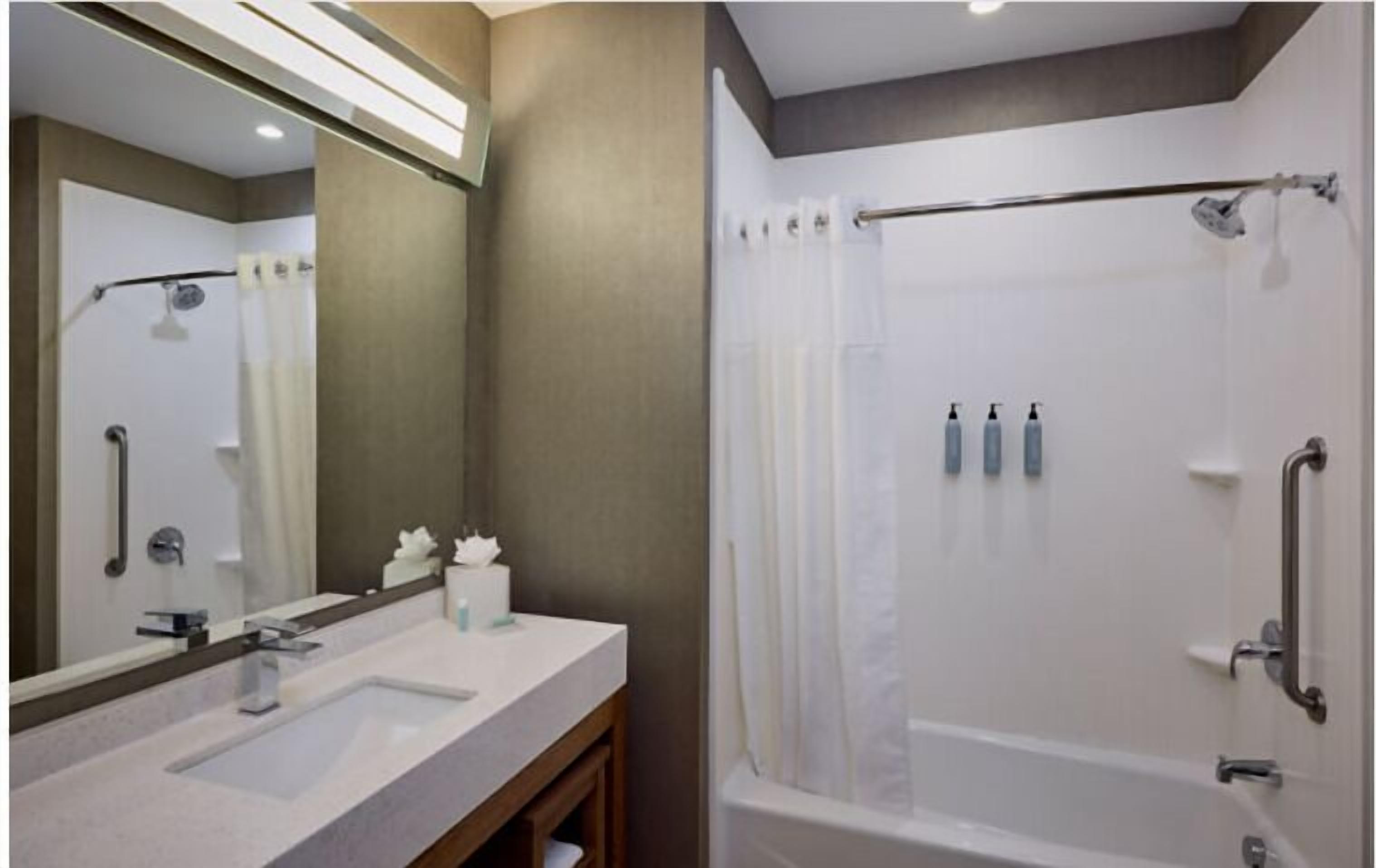 A bathroom with a sink, mirror, and shower area.