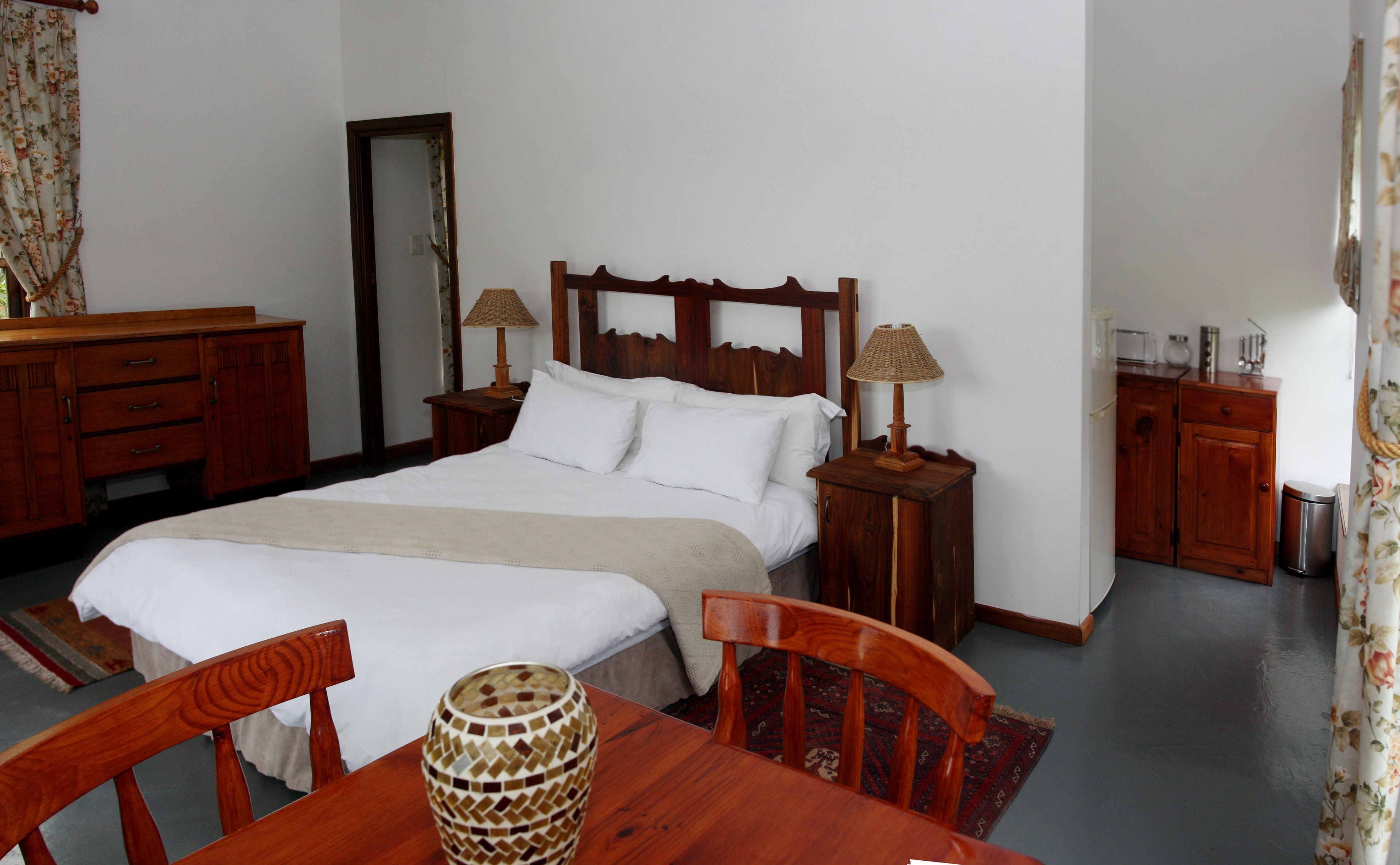 A neatly arranged bedroom with a bed, two bedside tables with lamps, a wooden dresser, a chair, and a table with a decorative vase.