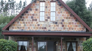 Une maison en pierre avec un porche, une chambre visible de l’extérieur et un chemin menant à l’entrée.