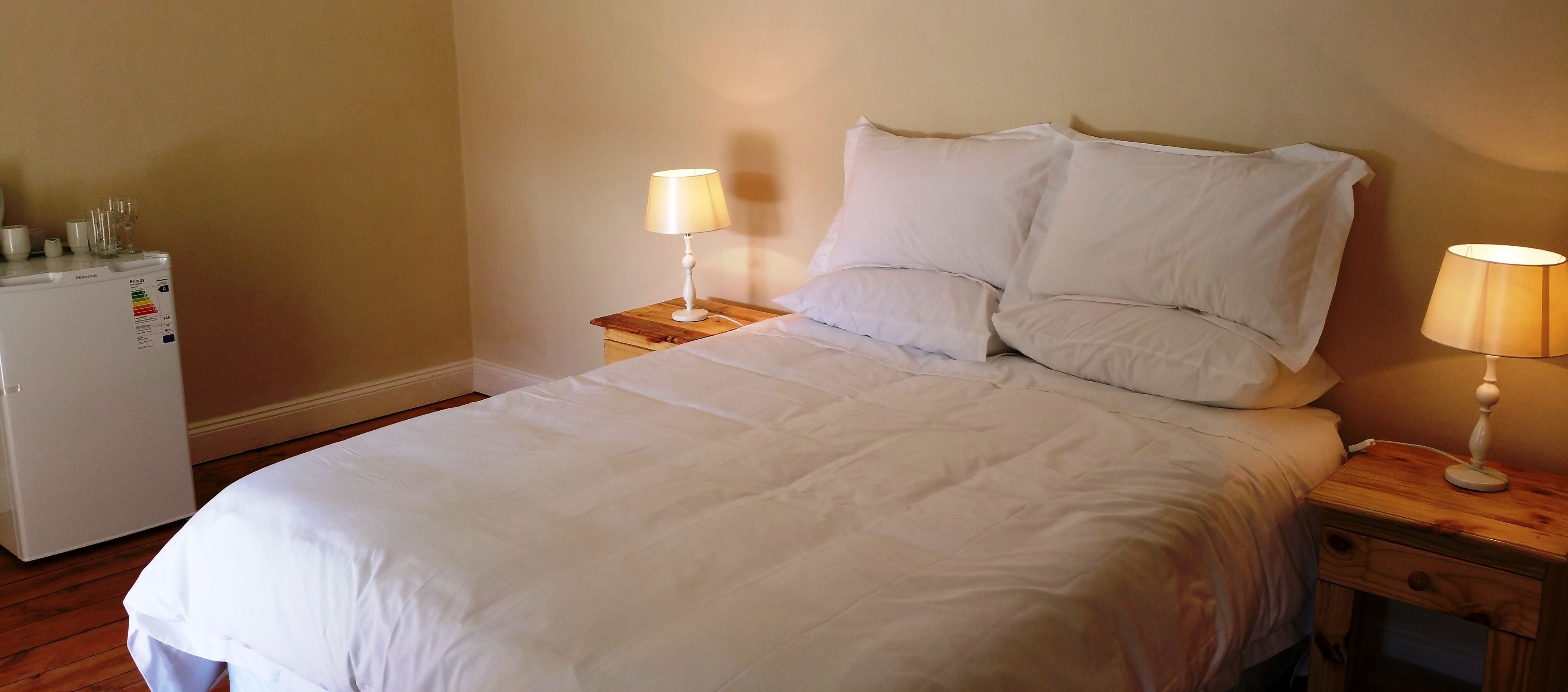 A neatly made bed with white linens, two bedside lamps, and a small wooden nightstand with a lamp.